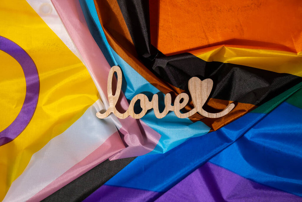 Wooden word love with heart romance on Rainbow LGBTQIA flag made from silk material. Valentine's Day greeting card. Symbol of LGBTQ pride month. Equal rights. Peace and freedom. Support LGBTQIA community. Diversity equality - Foto, afbeelding