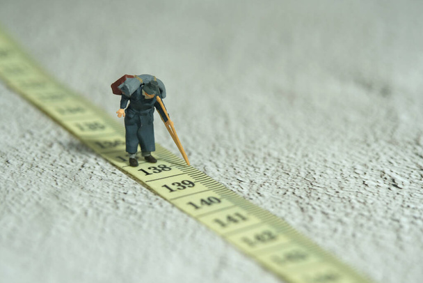 Miniature people toy figure photography. An old men grandfather walking above measuring tape. Distance traveled concept. Image photo - Fotografie, Obrázek