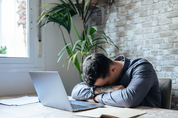 Exhausted young Caucasian male employee sleep desk at office overwork preparing report. Tired male fall asleep doze off at workplace, work late to meet deadline. Fatigue, exhaustion concept. - Photo, Image