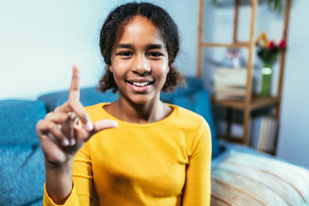 Улыбающаяся чернокожая девушка с языком жестов дома - Фото, изображение