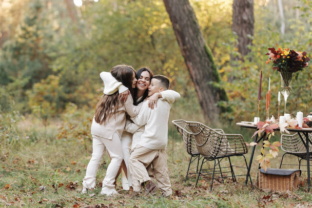 母の日。10代の娘と小さな息子を持つ幸せな若い母親は、秋の公園で楽しさと抱擁をしています。家族の日だ。休日にピクニックをしている牧歌的なスタイリッシュな家族。幸せな子供時代 - 写真・画像