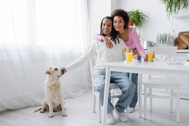 Smiling african ameican couple looking at camera near breakfast and labrador at home  - Fotografie, Obrázek