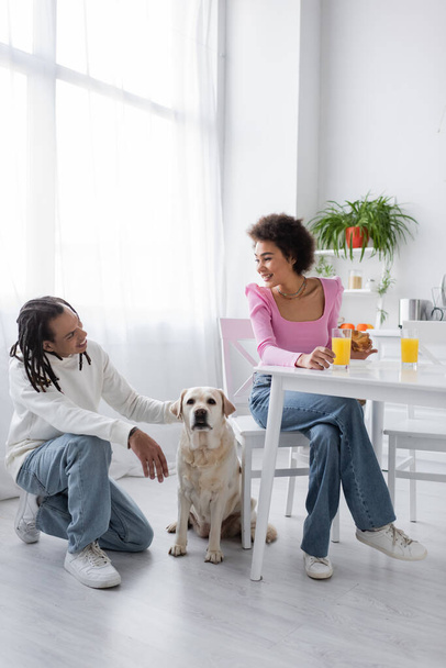 African american couple talking near labrador during breakfast in kitchen  - Foto, afbeelding