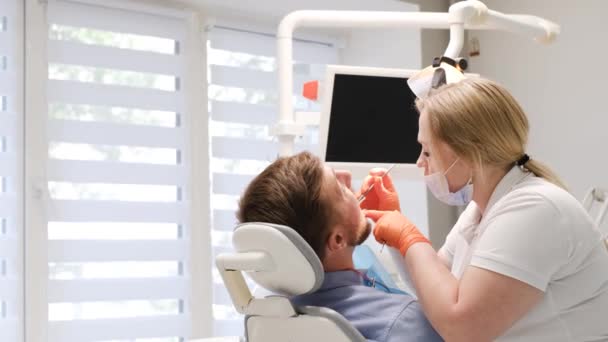 Profesionální zubař zkoumá mužské zuby. Pojetí zubního ošetření, odstranění zubního kamene, čištění zubního kamene. Moderní stomatologie USA - Záběry, video