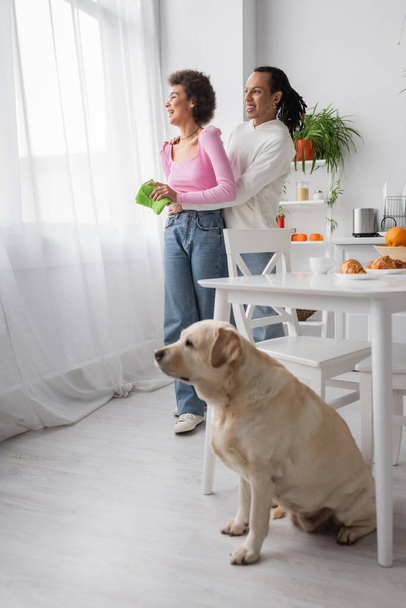 African american woman holding rag near boyfriend and blurred labrador at home  - Foto, Imagem