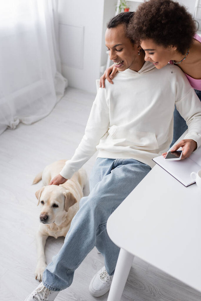 High angle view of smiling african american couple looking at labrador at home  - Photo, image