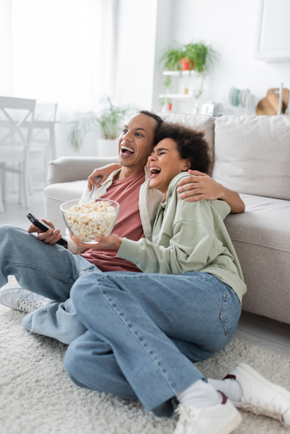 opgewonden afrikaanse amerikaanse paar met popcorn kijken comedy film thuis  - Foto, afbeelding