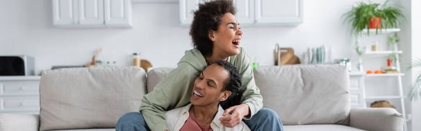 Emocionada mujer afroamericana abrazando novio mientras se sienta en el sofá en casa, pancarta  - Foto, imagen