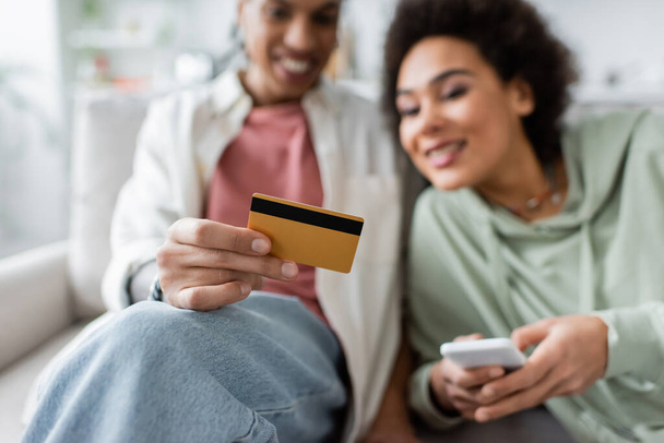Bulanık Afrikalı Amerikalı çift evde akıllı telefon ve kredi kartı kullanıyor.  - Fotoğraf, Görsel