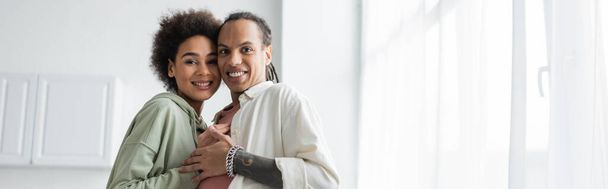 African american couple hugging and looking at camera in kitchen, banner  - Foto, Imagem