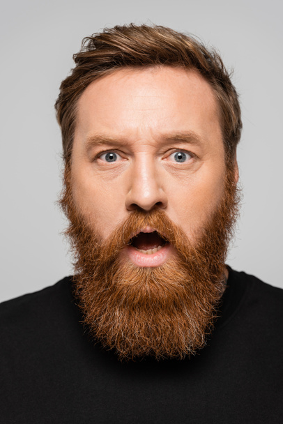 портрет шокированного бородатого человека с открытым ртом, смотрящего на камеру, изолированную на сером - Фото, изображение