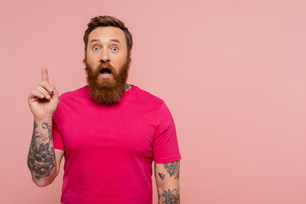 elképedt tetovált férfi bemutató ötlet gesztus, miközben áll nyitott szájjal elszigetelt rózsaszín - Fotó, kép