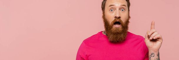 elképedt szakállas férfi fényes magenta pólóban ötlettáblát mutat elszigetelt rózsaszín, banner - Fotó, kép
