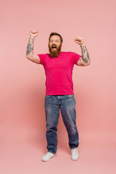 homme à la mode en t-shirt et jeans magenta se réjouissant et criant sur fond rose - Photo, image