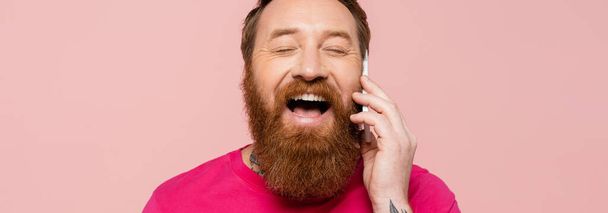 nevetés szakállas férfi csukott szemmel beszél okostelefon elszigetelt rózsaszín, banner - Fotó, kép