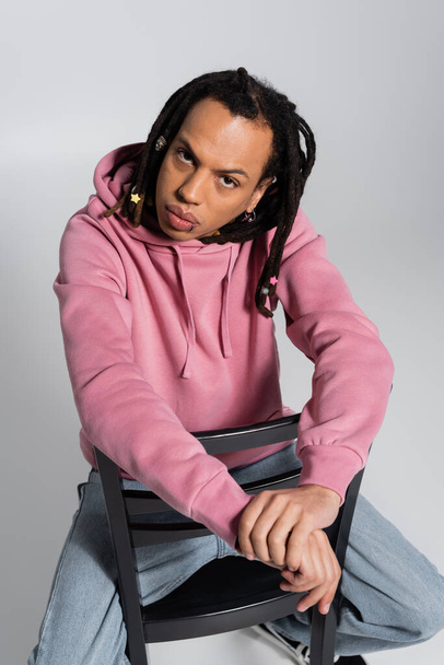 overhead view of multiracial man with dreadlocks sitting on chair and looking at camera isolated on grey  - Foto, afbeelding