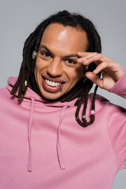 portrait of happy multiracial man in pink hoodie looking at camera isolated on grey  - Valokuva, kuva