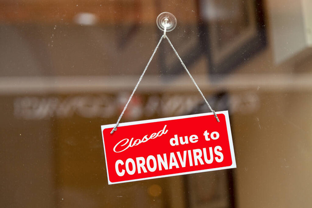 Красная вывеска висит на стеклянной двери магазина с надписью "Закрыто из-за коронавируса". - Фото, изображение