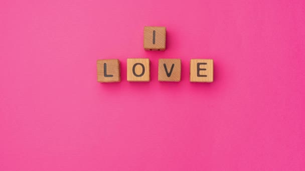 Drewniane kostki stop-motion ze zwrotem I Love You Może na pustym kolorowym różowym tle. Słowa miłości są zrobione z liter z drewna na Walentynki i dla swojej dziewczyny, chłopaka, żony - Materiał filmowy, wideo