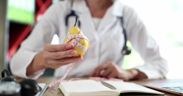 El médico dietista tiene pera amarilla y cinta métrica en la mano. El médico aconseja comer alimentos saludables con vitaminas - Metraje, vídeo