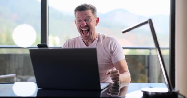 Happy freelancer businessman celebrating opportunity to receive great news via email. Excited man looking at laptop screen with clenched fists feeling happiness and success - Záběry, video