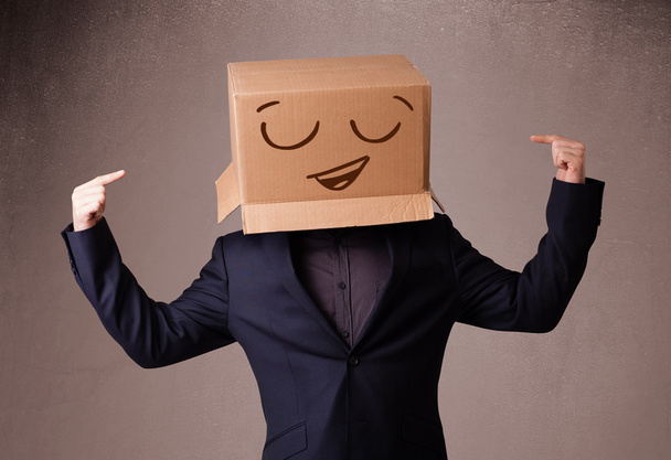 Young man gesturing with a cardboard box on his head with smiley - Foto, afbeelding