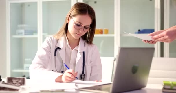 Kadın pratisyen doktor belgeleri imzalar ve hastaya teslim eder. Tıbbi belgelerin ve sigortanın kaydı - Video, Çekim