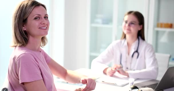 Kaunis onnellinen naispotilas, joka näyttää peukaloa lääkärin vastaanotolla klinikalla. Laadukas ammatillinen sairaanhoito ja vakuutus - Materiaali, video