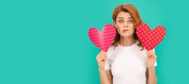 confused young girl with red heart on blue background. Woman isolated face portrait, banner with mock up copyspace - Photo, Image