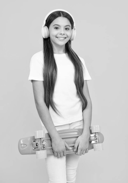 Happy teenager portrait. Teen hipster girl skater with skateboard and headphones on isolated background. Summer kids trend, urban teenage style. Smiling girl - 写真・画像