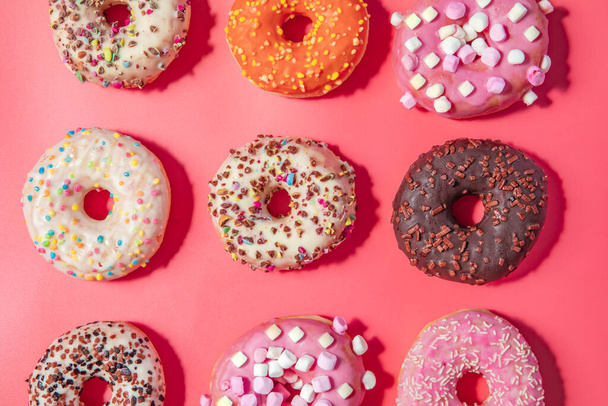 Donuts con glaseado sobre fondo rosa pastel. Dulces rosquillas. vista superior surtido con varios vidriados de chocolate y espolvoreos, caramelos concepto dulces de azúcar - Foto, imagen