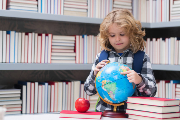 School kid pupil looking at globe in library at the elementary school. World globe. School child 7-8 years old with book go back to school. Little student - Photo, Image