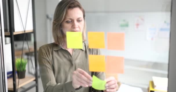 Confident manager plans to work on project. Business woman in office with glass partition glues colored leaves for effective project management - Séquence, vidéo