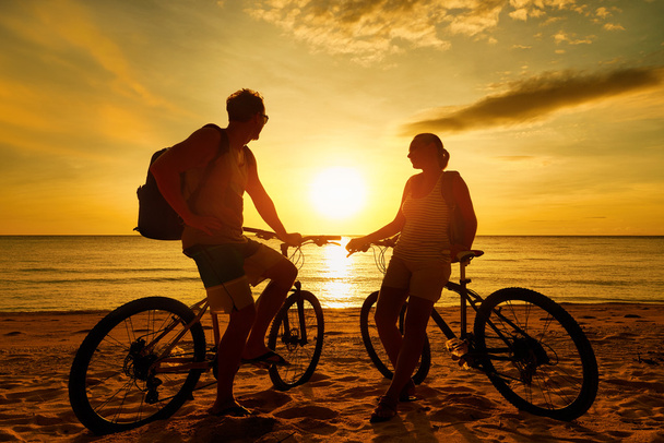Пара туристів з велосипеди спостерігаючи захід сонця. Силует людей - Фото, зображення