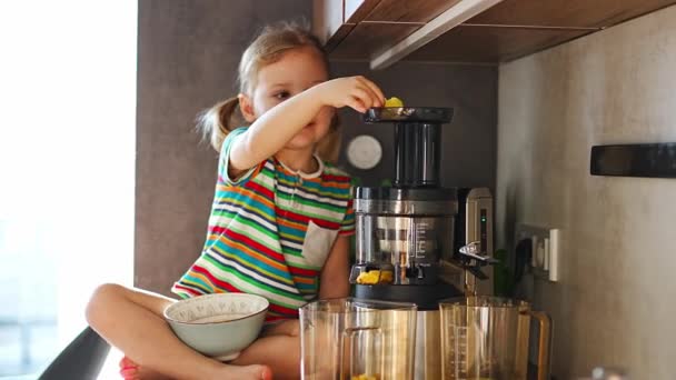 Little girl making fresh juice sitting on the table in home kitchen. High quality 4k footage - Imágenes, Vídeo