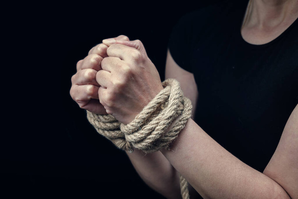 Siyah arka planda kabarık bir iple bağlanmış bir kadının elleri. Şiddet kavramını istismar etmeyi bırak - Fotoğraf, Görsel