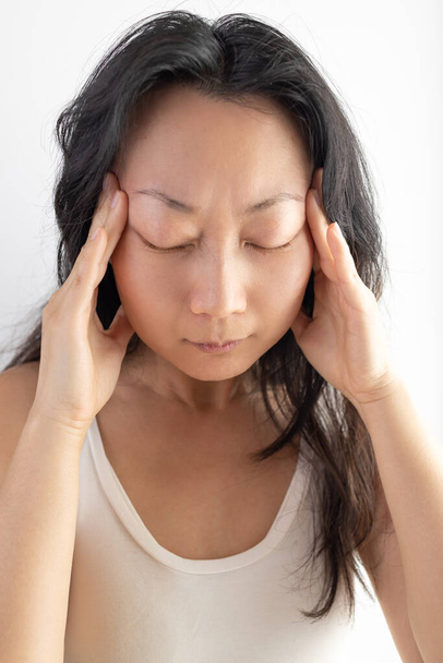 Young Asian girl wearing casual white T-shirt over isolated background suffering from headache desperate and stressed because pain and migraine. Hands on head. - Photo, image