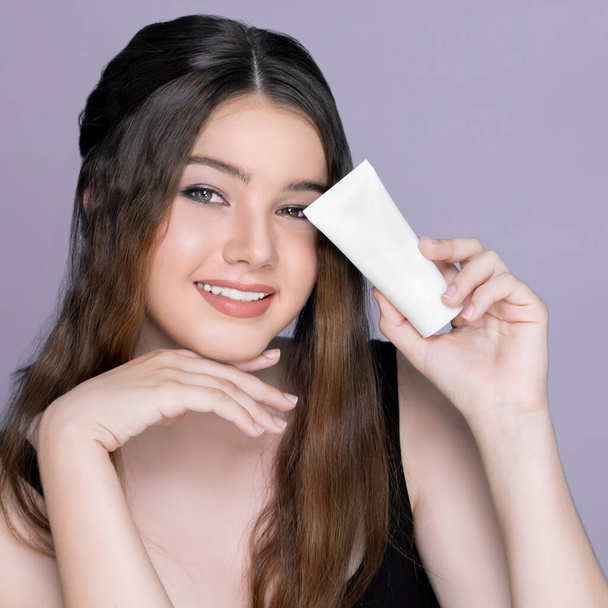 Young charming girl hold mockup moisturizer skincare cream tube or container for copyspace advertising. Photo of beautiful and attractive girl with perfect makeup for beauty concept. - Photo, image