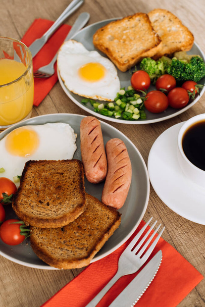 Αγγλικό πρωινό με καφέ και χυμό πορτοκάλι, λουκάνικο σχάρας και φρυγανισμένο ψωμί ολικής αλέσεως με τηγανητό αυγό και ντοματίνια στο πιάτο - Φωτογραφία, εικόνα