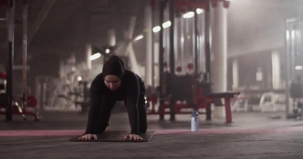Handheld shot of Muslim female athlete doing Extended Child and Cobra poses to stretch back during fitness training in gym - Metraje, vídeo