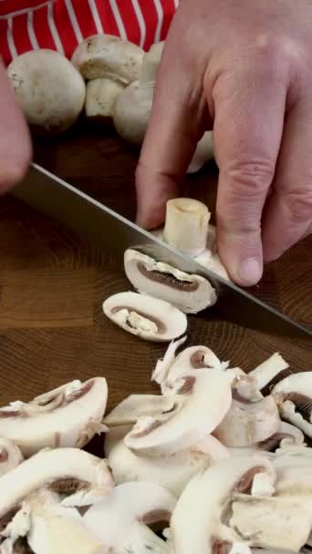 Chefs hands slicing button mushrooms with sharp knife into pieces on chopping board. Cooking vegetarian or vegan food on domestic kitchen. Vertical. Close up. - Séquence, vidéo