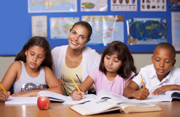 Naše mládí napíše naši budoucnost. Mladá učitelka sedící se svými třemi etnickými žáky při studiu - portrét - Fotografie, Obrázek
