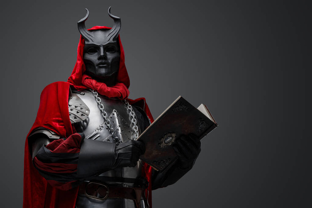 Πορτρέτο του κακού ιππότη με το βιβλίο ντυμένο με κόκκινη ρόμπα και πανοπλία πλάκα. - Φωτογραφία, εικόνα