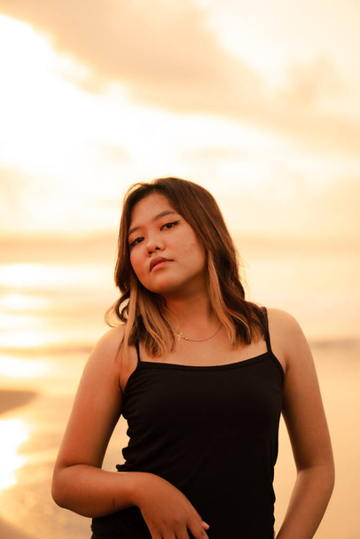 een blonde Aziatische vrouw met een mooi gezicht en zwarte kleren genieten van de schoonheid van het strand en de golven in de ochtend voor zonsopgang - Foto, afbeelding