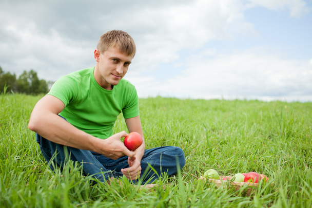 Young man sitting on the grass with apple - Фото, зображення