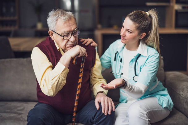 Nurse home caregiver is assisting old man at his home. Professional health support for elderly people. - Photo, image
