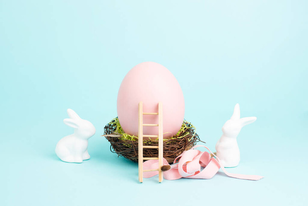 鳥の巣、ギフトリボンとはしご、春の休日に巨大なピンク色の卵の横に座っているイースターウサギやウサギ - 写真・画像