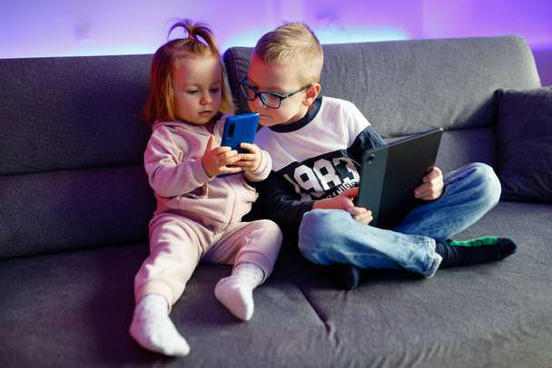 Danya e sua irmã mais nova Emilia brincam com celulares e tablets. As crianças estão constantemente sentadas em telefones e tablets. - Foto, Imagem