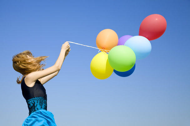 Руда дівчина з кольоровими кульками на фоні блакитного неба
. - Фото, зображення