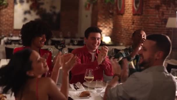 gruppo di amici riuniti a cena nel ristorante applaudono - amici multirazziali a cena applaudendo e sorridendo in terrazza - Filmati, video